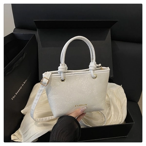 Detailed view of white snake-embossed tote bag with golden hardware and fashion logo