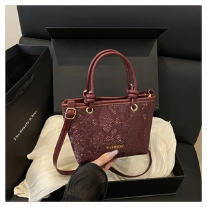 Close-up of burgundy snake pattern handbag with gold hardware and a fashion gift box