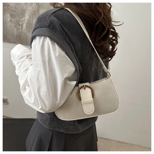 Detail of light beige baguette bag with bronze circular buckle on model shoulder