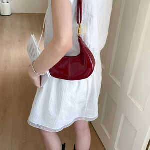 Deep burgundy patent leather hobo bag with gold hardware shown on a model