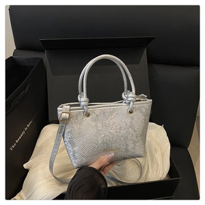 Detail of silver snake-embossed mini tote bag with gold logo on white silk fabric