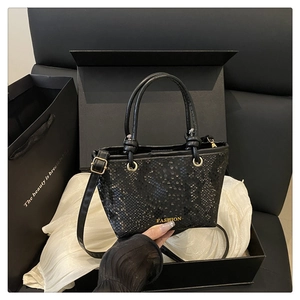 Detail of black snakeskin texture tote bag with gold logo in luxury gift box packaging