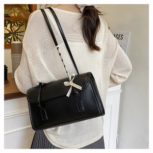 Detail of black glossy leather underarm bag with beige bow and woven strap on model