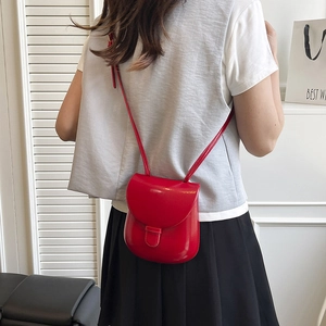 Classic red shiny leather saddle crossbody bag shown on model in minimalist setting