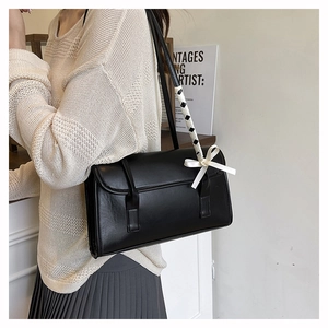 Detail of black leather underarm bag with decorative white silk bow and braided strap
