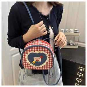 Détail du sac à dos à carreaux rouges avec patch cœur en jean, dentelle et étiquette cerise