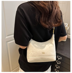 Détail du sac croissant blanc avec texture serpent et lettrage doré porté à l'épaule