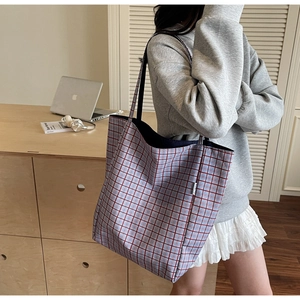 Detail of red and blue checkered fabric tote bag showing a white label and thin shoulder strap