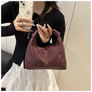 Détail d'un sac à main bordeaux texture crocodile avec logo doré porté par un modèle