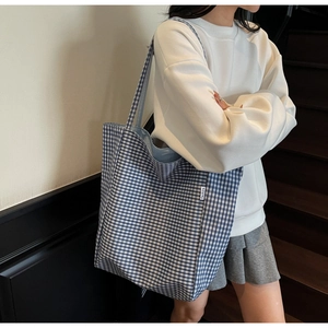 Detail of blue and white checkered tote bag featuring a small white fashion woven label