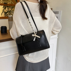 Minimalist black faux leather shoulder bag with decorative woven strap and bow accent