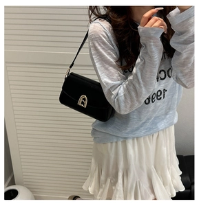 Détail d'un sac bandoulière en cuir noir avec boucle dorée arquée porté par un mannequin