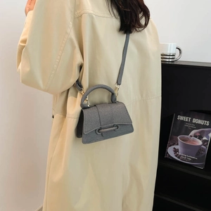 Minimalist grey mini crossbody bag with top handle and gold hardware on a beige trench coat
