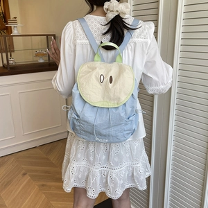 Blue aesthetic backpack with apple-shaped flap and cute eyes in a lifestyle cafe setting
