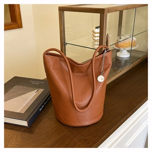 Detailed macro view of brown lychee grain leather bucket bag with silver charm pendant