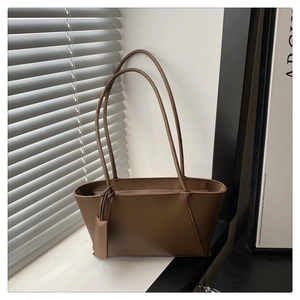 Detail of a brown leather trapezoid tote bag with slender straps in natural window light