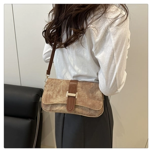 Sac baguette en cuir mat marron avec texture et boucle dorée porté à l'épaule