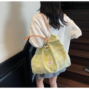 Detail of green plaid tote bag featuring drawstring closure and woven shoulder strap