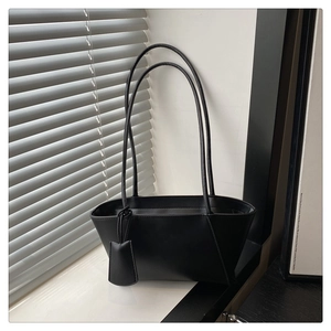 Close-up of minimalist black tote bag with long shoulder strap and chic square pendant