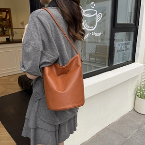 Minimalist brown lychee leather bucket bag shown in a stylish outdoor street fashion setting