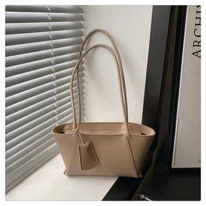 Close-up of the beige minimalist leather handbag with slender handles on a studio window sill