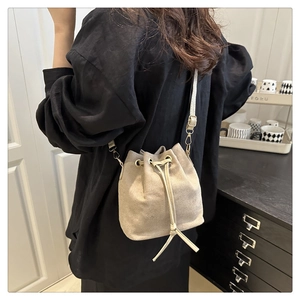 Close-up of beige suede drawstring bucket bag with gold hardware worn as a crossbody