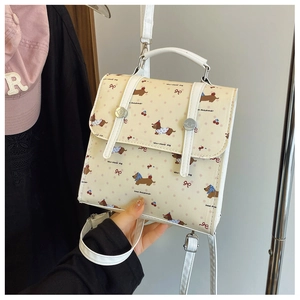 Close-up of cream square backpack featuring cartoon dachshund and cherry patterns