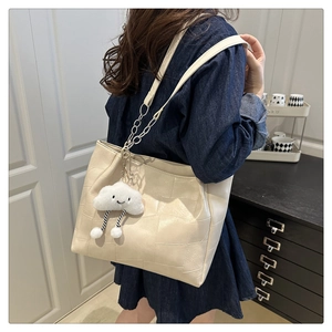 Detail of a beige tote bag with pebbled leather texture and cloud plush charm