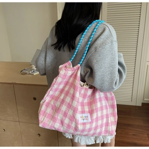 Detail of pink plaid tote bag with braided blue shoulder strap and white label