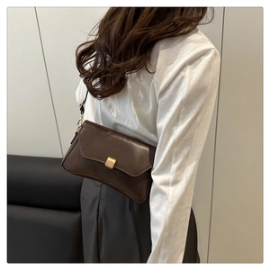 Dettaglio borsa sottobraccio in pelle marrone scuro con fibbia dorata su top bianco