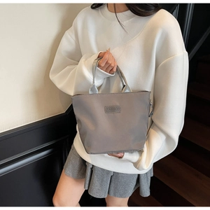 Detail of grey nylon handbag with FASHION label held by model in casual outfit