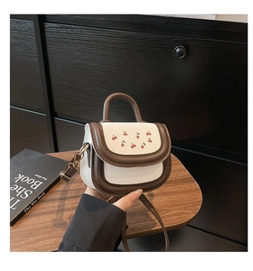 Détail du sac bandoulière avec broderie cerise et finitions marron élégantes