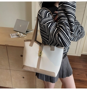 Detail view of contrast tote bag with gold lock buckle on a wooden office desk