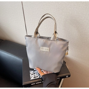 Dettaglio della borsa grigia in nylon con etichetta moda e manici dorati in metallo lucido