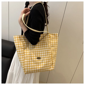 Detailed shot of yellow plaid canvas tote bag with handmade metal tag and woven handles