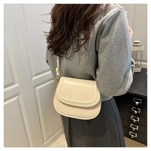 Detailed side view of off-white saddle bag with golden metal buckle on model