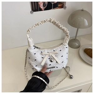 Detail view of white ruched leather bucket bag with black bow print and heart pendant