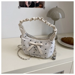 Detail of quilted bucket bag with bow prints and cloud pleated handle on beige counter