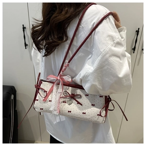 Détail d'un sac sous le bras en toile avec motif nœud rouge et pendentif cœur à l'épaule