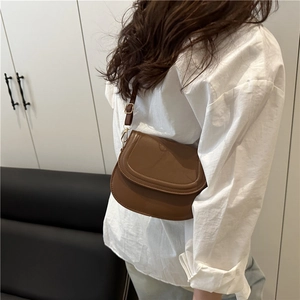 Chic brown synthetic leather saddle bag worn crossbody with adjustable shoulder strap