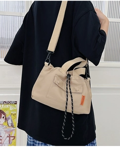 Detail of beige nylon tote bag with drawstring closure and orange woven brand tag