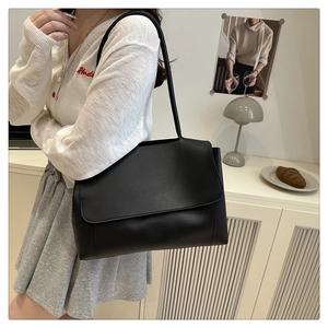 Detail view of a black leather tote bag with flap closure and long shoulder strap