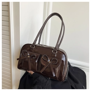 Detail of dark brown glossy patent leather bag with bow-decorated front flap pockets