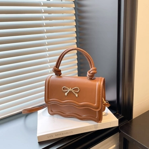Elegant brown leather shoulder bag with gold bow ornament and wavy flap detail