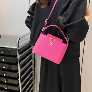 Sac bandoulière en cuir magenta avec fermoir en V doré porté par un mannequin de mode