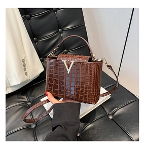 Detail view of brown crocodile texture handbag with silver V-buckle and adjustable strap