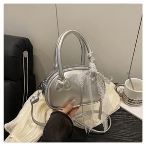 Silver metallic crossbody bag with lace bow detail and adjustable strap on a soft sofa