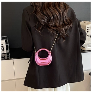 Metallic pink acrylic crossbody bag with gold chain shown on a model's shoulder