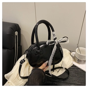 Close-up of a black glossy crossbody bag with bow texture and elegant lace ribbon charm