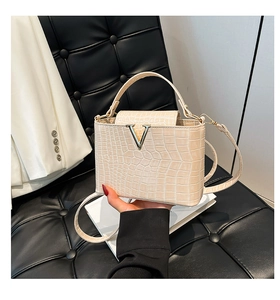 Detail of crocodile embossed cream handbag with V-shaped metal clasp on leather seat